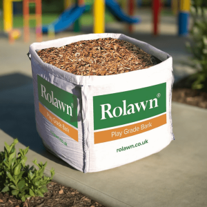 Rolawn play grade bark bulk bag sat on a concrete path with a colourful play area behind that has a play bark safety surface to protect children from falling